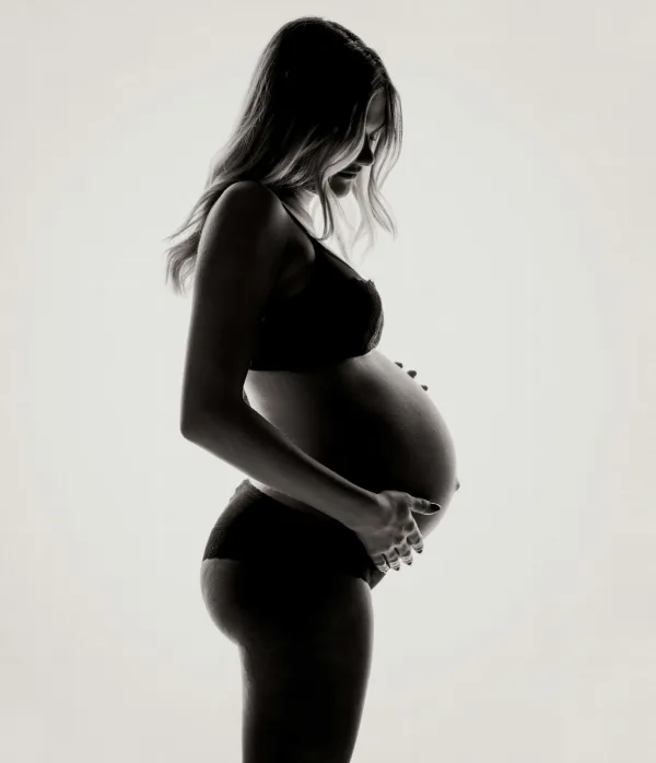 A pregnant woman in silhouette holding her belly against a bright white background