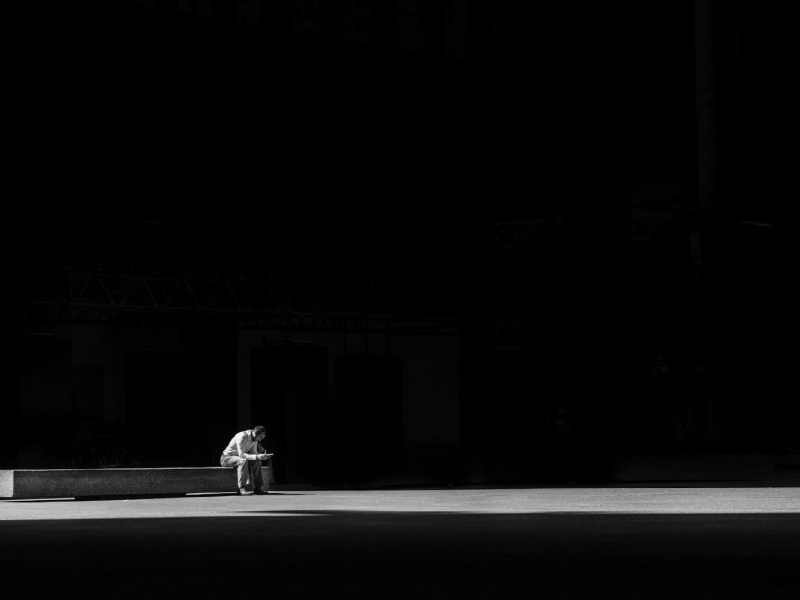 grayscale photogaphy of man sitting on concrete bench